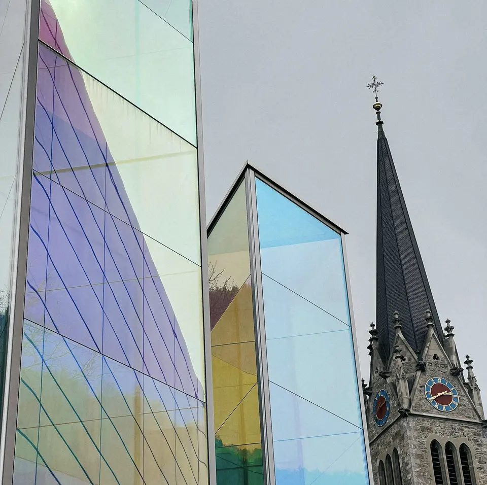 Modern church with colorful glass reflections and traditional steeple.